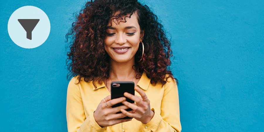 Beautiful young woman with dark curly hair smiling at the message on her phone.