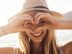 Attractive blonde female peering through her hands which are shaped like a heart