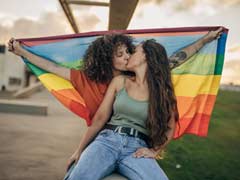 Lesbian couple kissing whilst holding onto the LGBTIQ rainbow flag